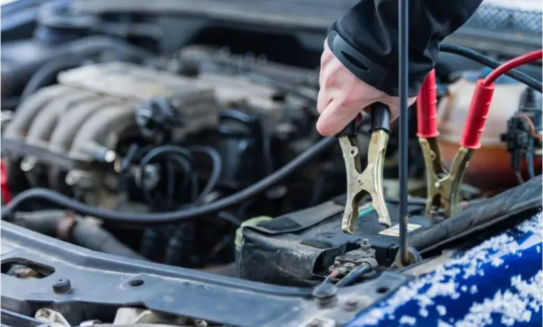 Ruce připojují kabely k vybité autobaterii pod kapotou auta.