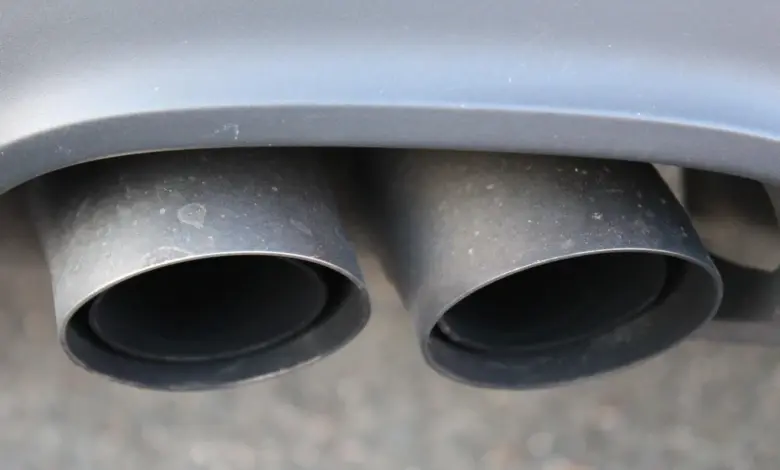 Dvě černé výfukové trubicí automobilu pod šedým nárazníkem.