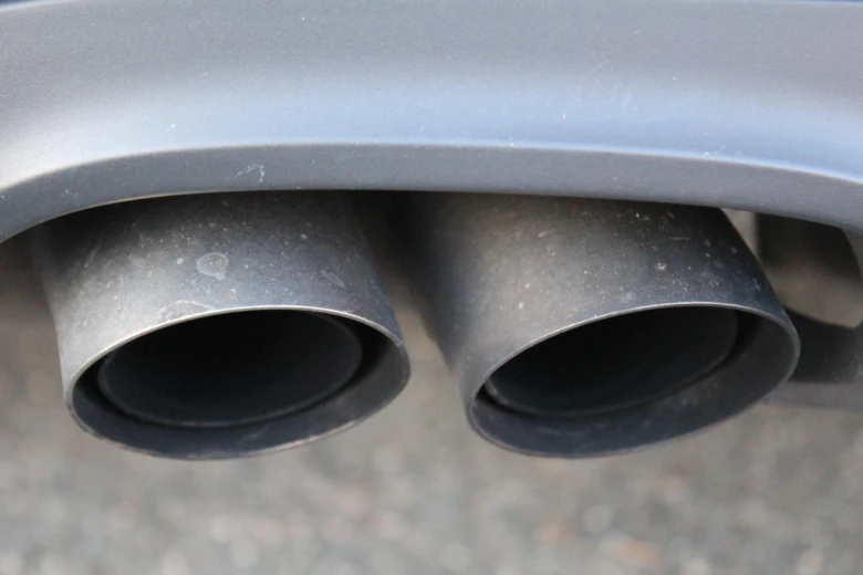 Dvě černé výfukové trubicí automobilu pod šedým nárazníkem.