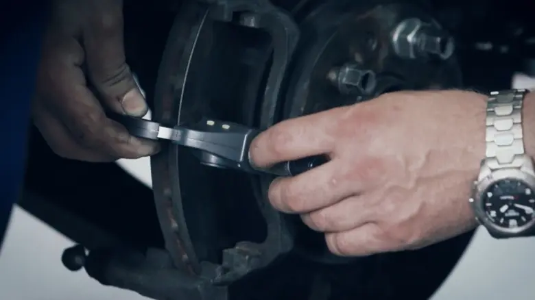 Mechanik měří minimální tloušťku brzdového kotouče pomocí kalibru.