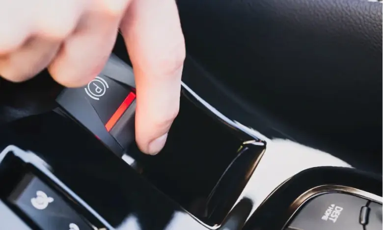Ruka tlačí na vypínač elektrické parkovací brzdy v autě.