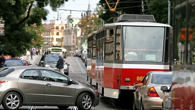 Červená tramvaj stojí v provozu mezi auty na ulici.