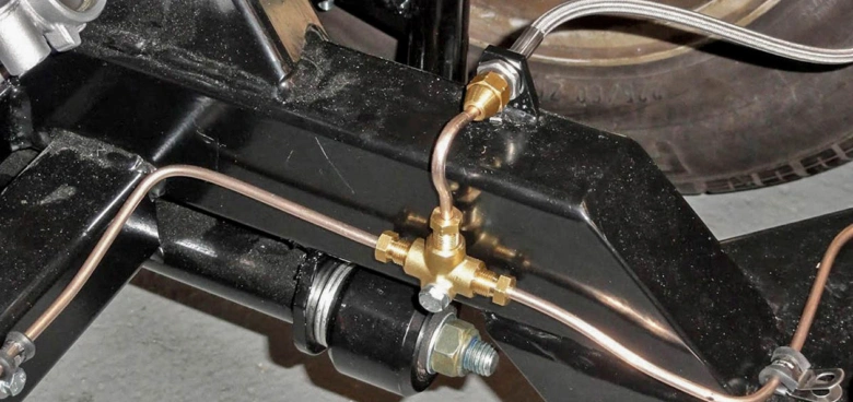 Detailní pohled na měděné brzdové potrubí u kola vozu.