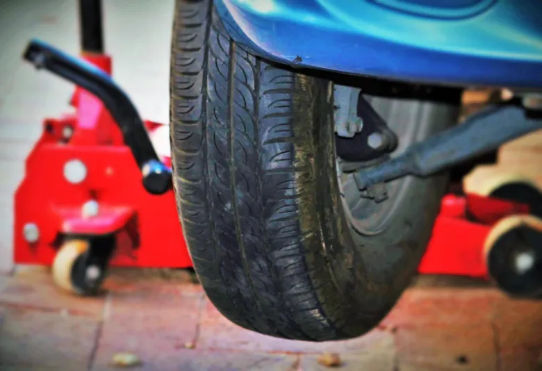 Modré auto zvednuté červeným hydraulickým zdvihačem.