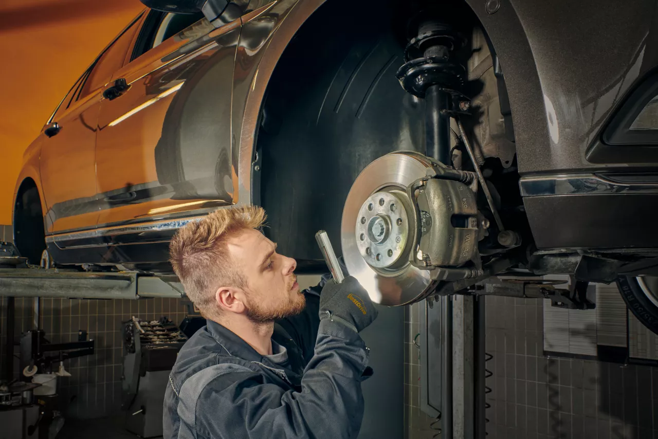 Mechanik opravuje brzdný systém u zvednutého vozu v dílně.