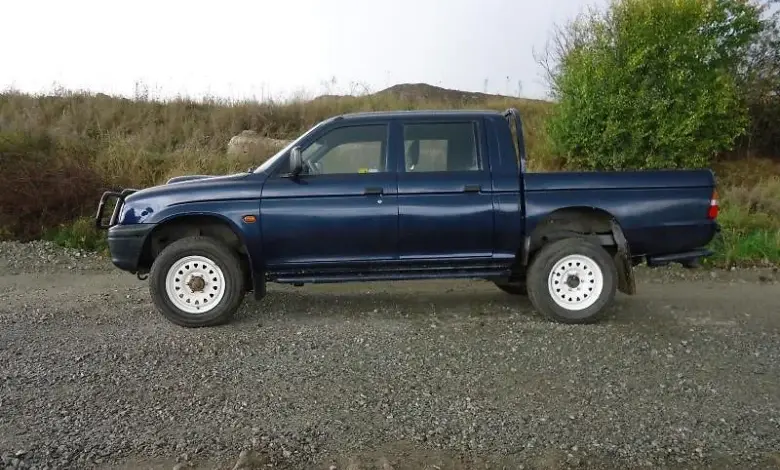 Modrý Mitsubishi L200 dvoudveřový pick-up stojící na štěrkové ploše.