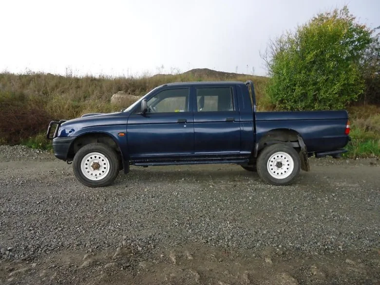 Modrý Mitsubishi L200 dvoudveřový pick-up stojící na štěrkové ploše.