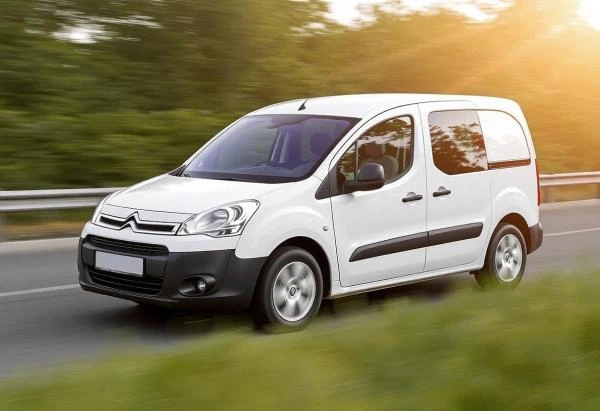 Bílý Citroën Berlingo jezdí po silnici v přírodě.