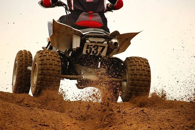 Čtyřkolka jede po blátivé svahu s výfukem.