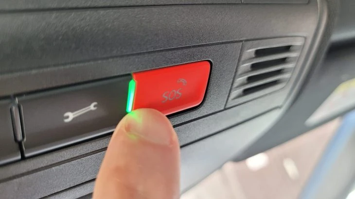 Prst tlačí červené SOS tlačítko v autě s zelenou kontrolní lampičkou.