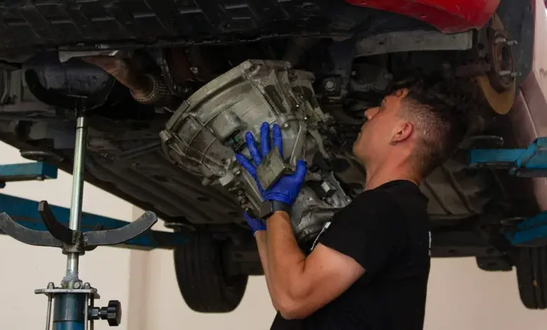 Mechanik drží převodovku pod autem při opravě.
