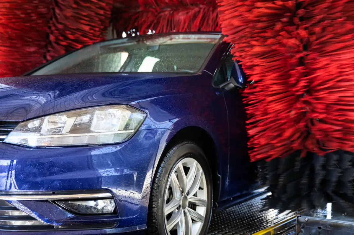 Modré auto v samoobslužné myčce s červenými kartáči.