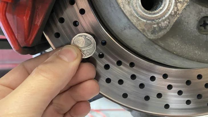 Ruka drží minci u brzdového kotouče při diagnostice pískání.