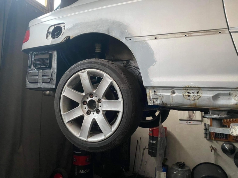 Bílé auto s poškozeným blatníkem na zvedáku v dílně.