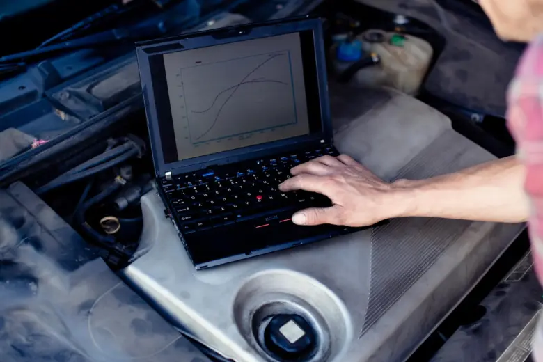 Laptop s grafy na motoru auta při diagnostice pro chiptuning