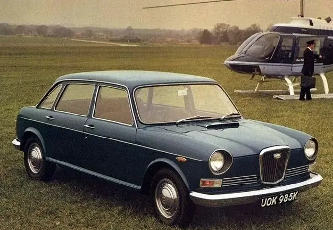 Modrý britský automobil z sedmdesátých let s vrtulníkem na pozadí.