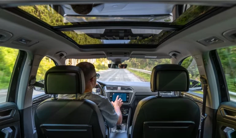 Muž řídí auto s panoramatickou střechou po silnici.