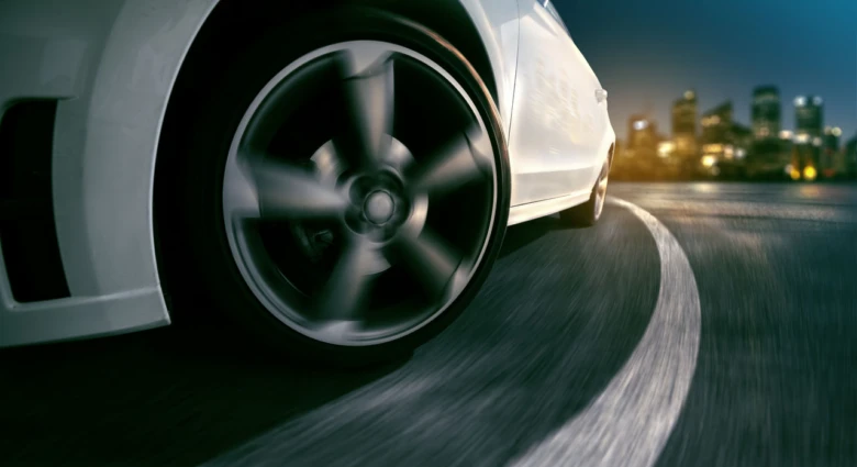 Bílý automobil v pohybu na noční silnici s městem.