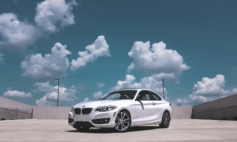Bílý automobil BMW na asfaltové ploše pod modrou oblohou.