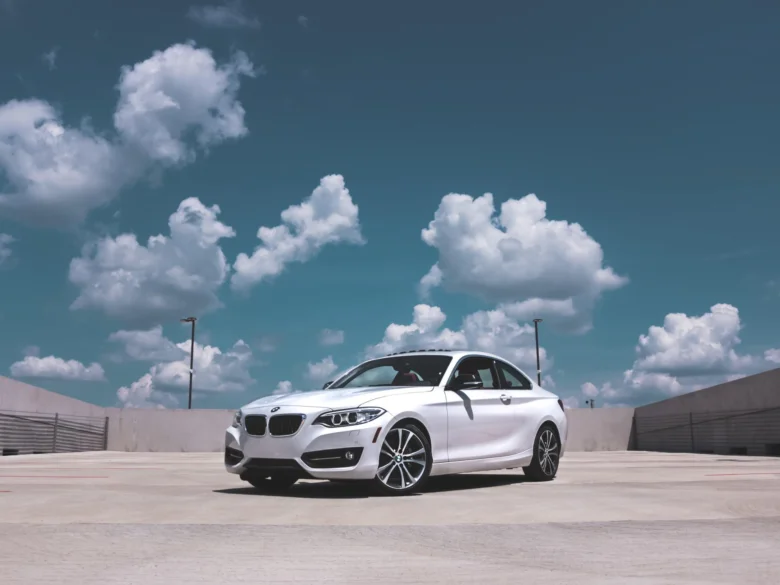 Bílý automobil BMW na asfaltové ploše pod modrou oblohou.