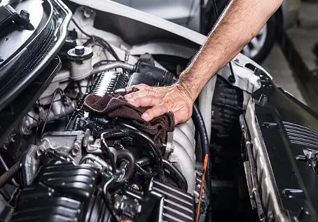 Muž čistí motor vozu hadříkem pod kapotou.