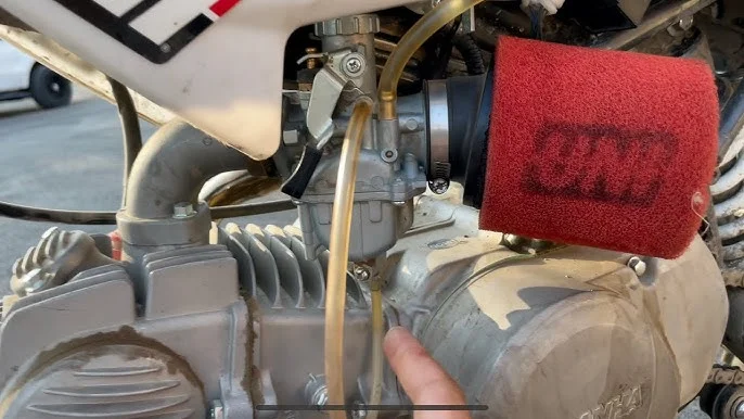 Detail motoru motocyklu s karburátorem a červeným filtrem vzduchu.
