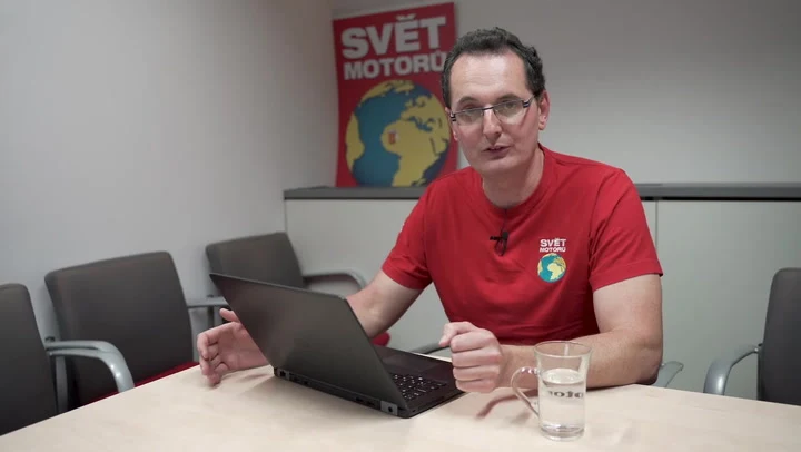 Muž v červeném tričku sedí u počítače s otevřeným notebookem.