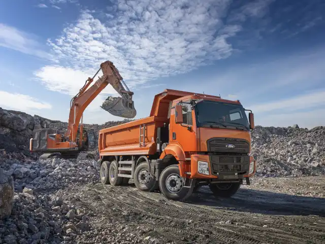 Oranžový nákladní automobil s vykopávačem na skládkě.