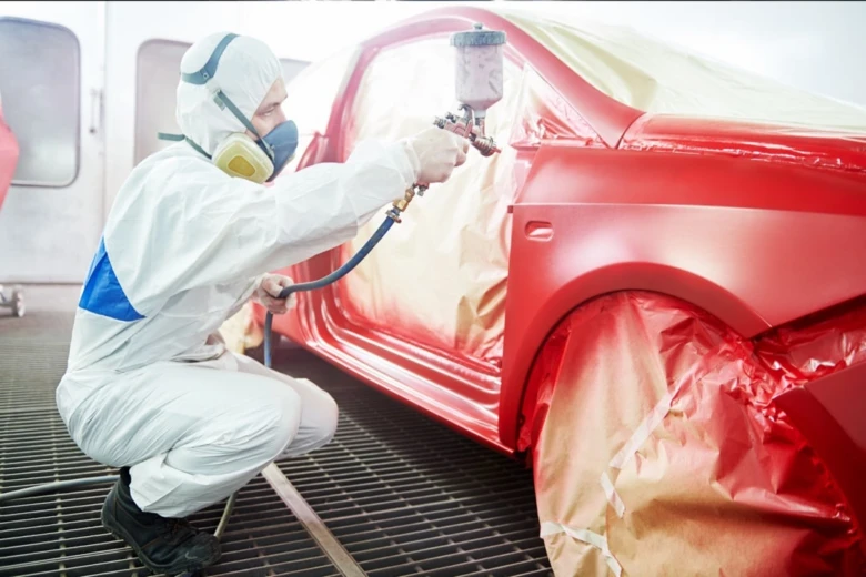 Profesionál lakuje červené auto v kabince bez poškození barvy.