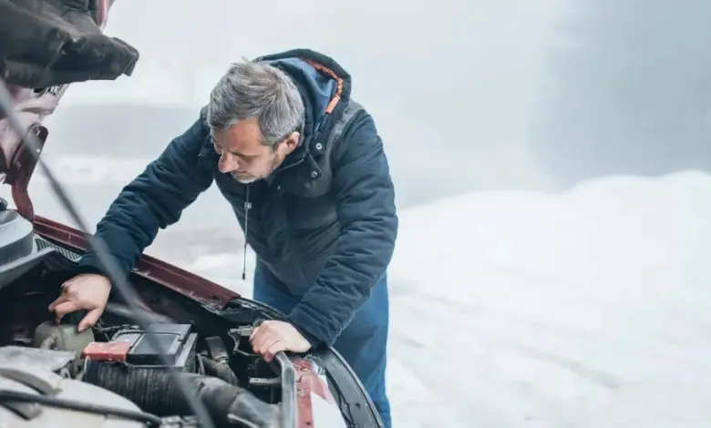 Muž kontroluje motor auta v zimě kvůli problémům se startováním.
