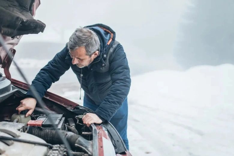 Muž kontroluje motor auta v zimě kvůli problémům se startováním.