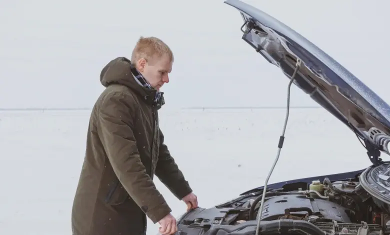 Muž kontroluje motor vozu v zimě s otevřenou motorkovou kapotou.