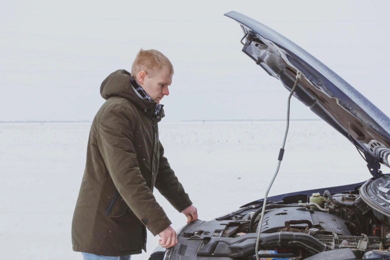 Muž kontroluje motor vozu v zimě s otevřenou motorkovou kapotou.