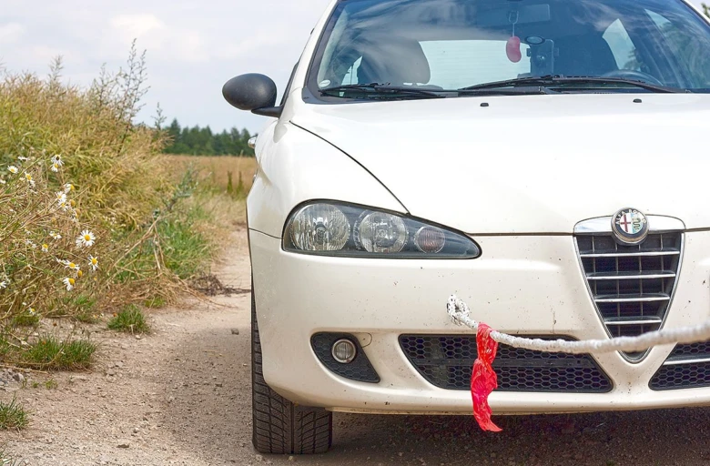 Bílý automobil připravený k tažení na venkovské cestě.