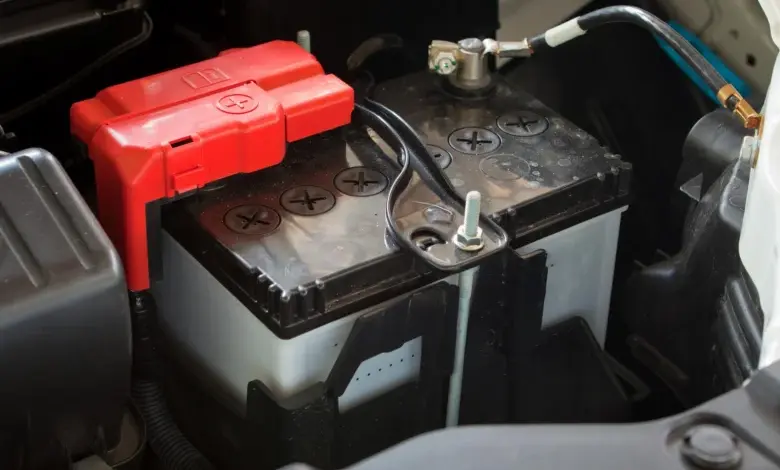 Autobaterie s červeným krytem kladného pólu pod kapotou.