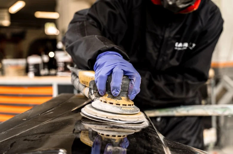 Pracovník opravuje puchýř na laku auta pomocí brusky.