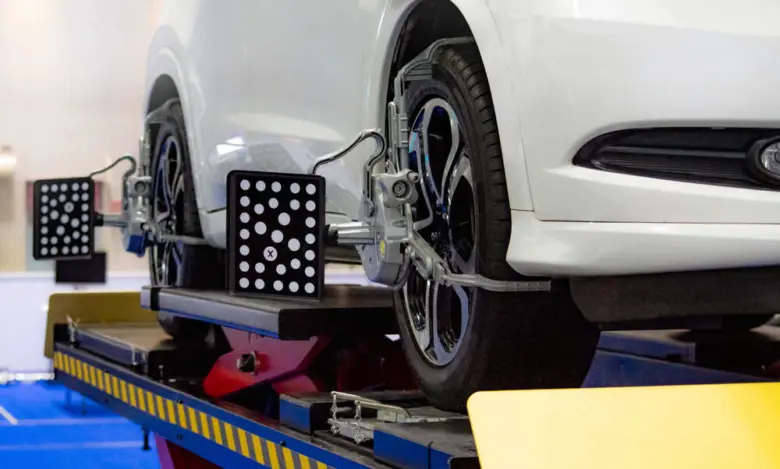 Bílý automobil na zvedáku s přístrojem pro nastavení geometrie.