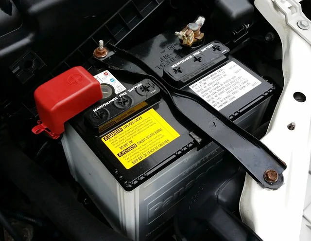 Autobaterie s viditelnými pólami a varovnými štítky pod kapotou.
