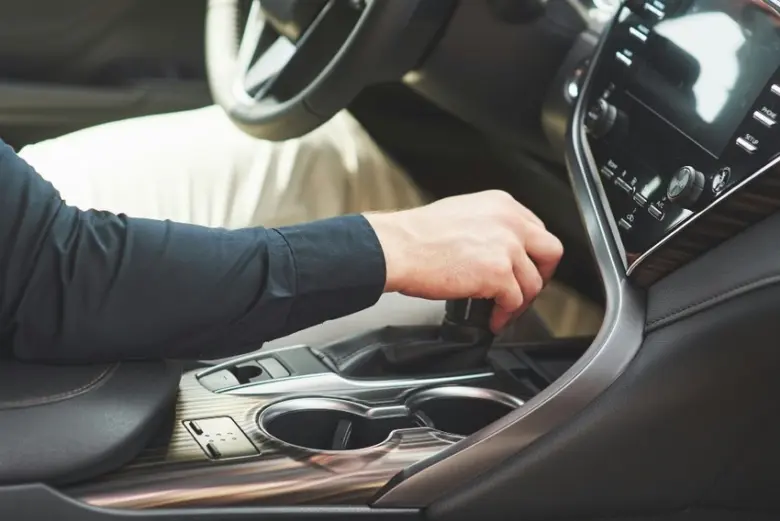 Ruka řidiče přepíná převodovku v autě s automatikou.