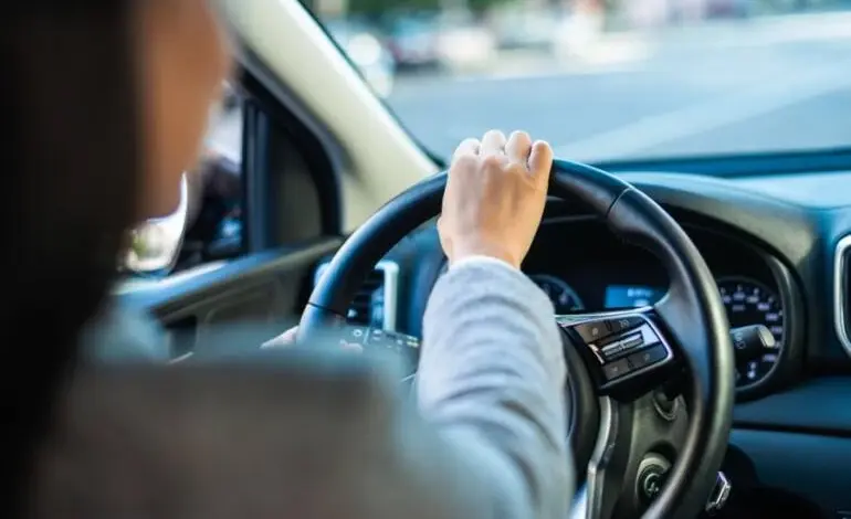 Osoba řídí automobil s volantem v rukou.