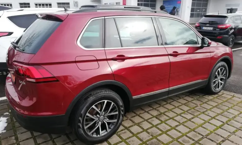 Červený SUV Volkswagen Tiguan zaparkovaný na dlažbě před prodejnou.