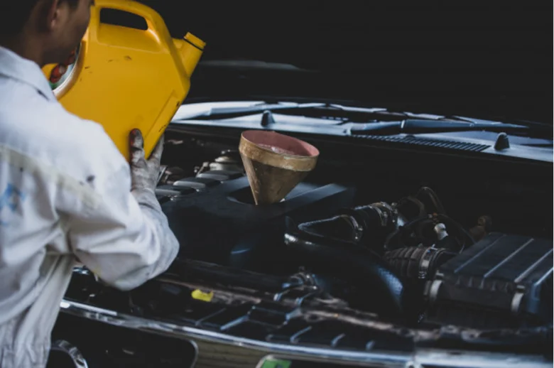 Mechanik nalévá olej do motora auta pomocí lejna.