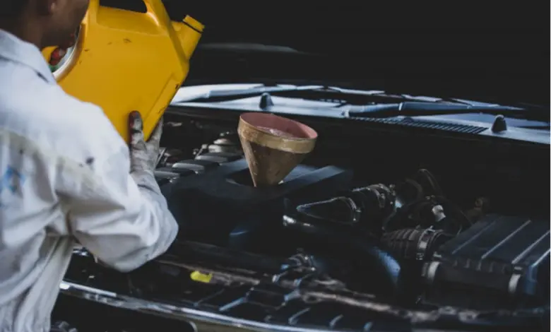 Mechanik nalévá olej do motora auta pomocí lejna.