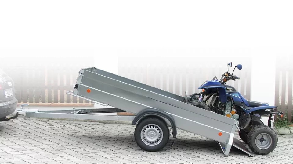 Přívěs pro motoblok s naloženým motocyklem na vozovce.