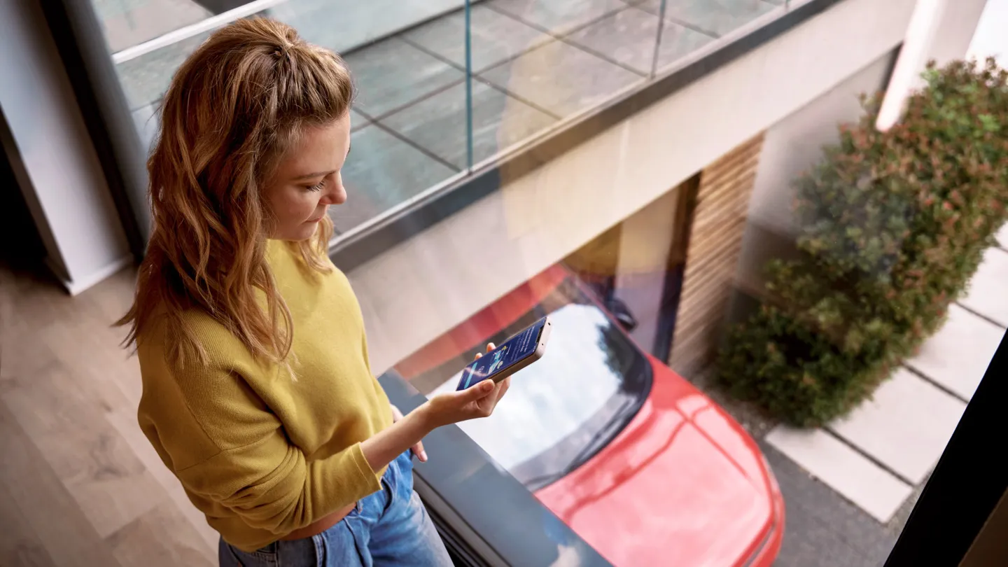 Žena používá aplikaci na mobilu u vozu značky VW.