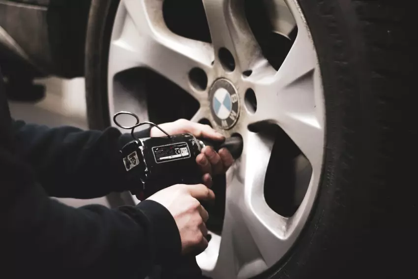 Mechanik odšrouvává kolo auta elektrickým klíčem.