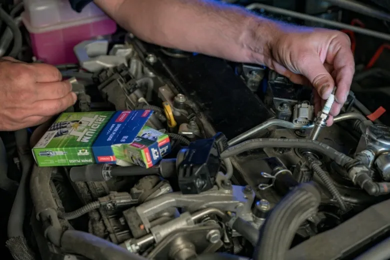 Mechanik mění svíčku v motoru s krabicí nových zapalovacích svíček.