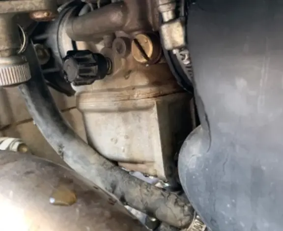 Blízký pohled na karburátor motocyklu s viditelnými šrouby pro nastavení.