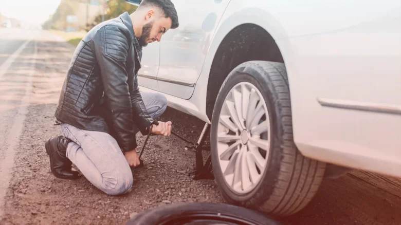 Muž mění auto na silnici pomocí zvedáku.