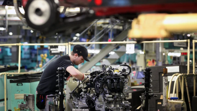 Pracovník montuje automobilový motor na výrobní lince v továrně.